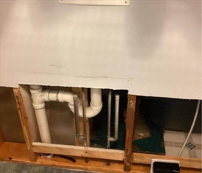 Washing machine hookups on a wall next to an outlet with flood-cut drywall and visible framing and plumbing underneath
