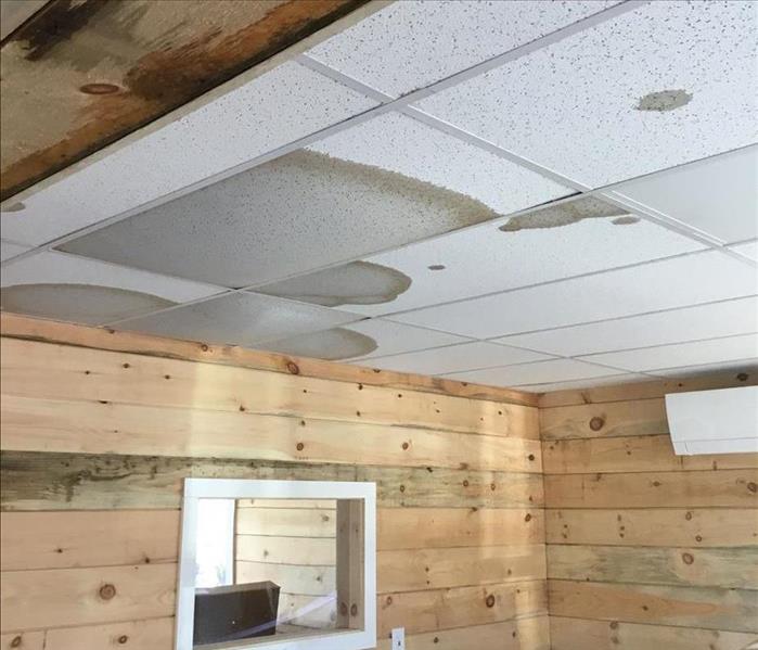 Water damage to a kitchen drop ceiling that is highly visible on wood and ceiling tiles